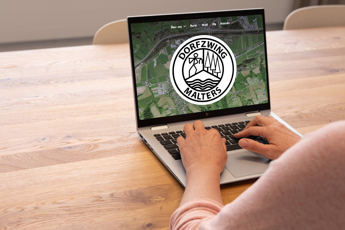 Eine Person benutzt einen Laptop, auf dem ein kreisförmiges Logo mit „Dorfzwing Malters“ und ein Symbol mit Gebäuden und einem Fluss angezeigt werden.