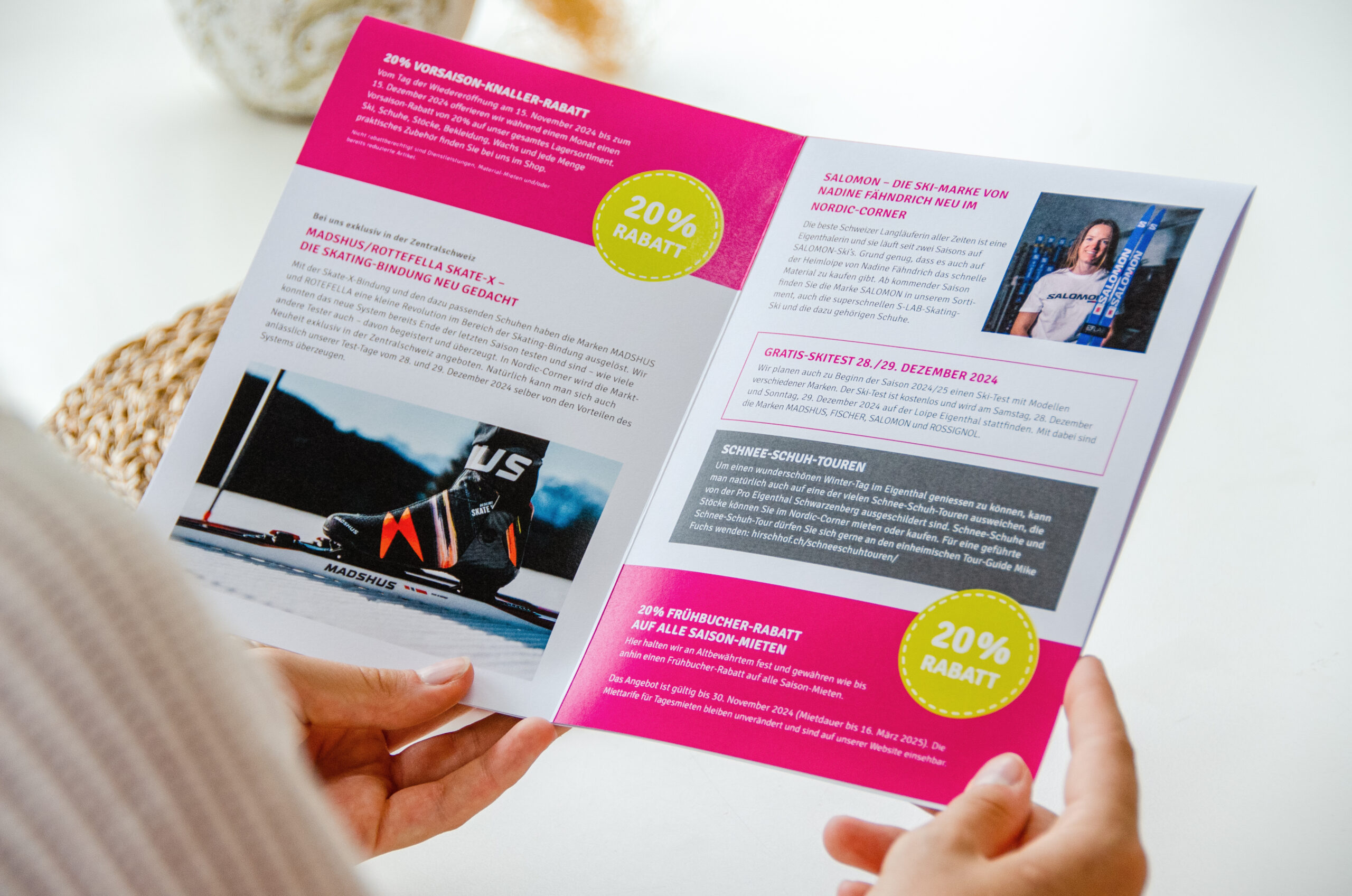 Eine Person hält eine aufgeschlagene Broschüre mit einem Segelboot-Bild und Werbetext in der Hand. Das Design ist rosa hervorgehoben, mit fettem Text versehen und in mehrere Abschnitte unterteilt. Kreisförmige Grafiken zeigen ein Angebot mit 20 % Rabatt. Ein Foto einer Person ist ebenfalls enthalten.