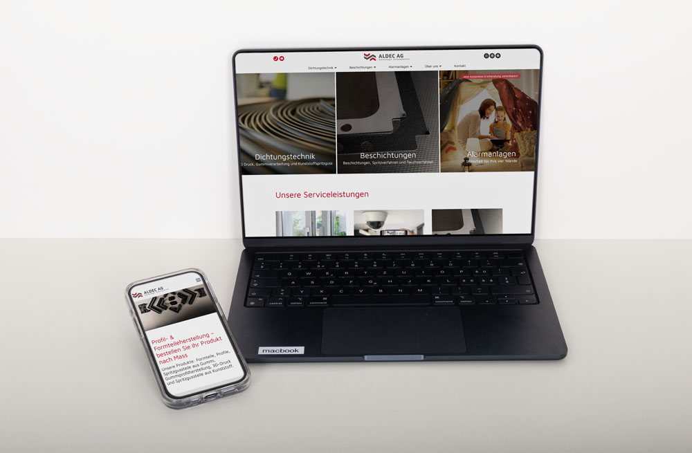 Ein MacBook zeigt eine Website mit Industrieanlagen in mehreren Bereichen. Daneben zeigt ein Smartphone eine entsprechende Webseite mit deutschem Text. Beide Geräte stehen auf einer hellen Oberfläche.