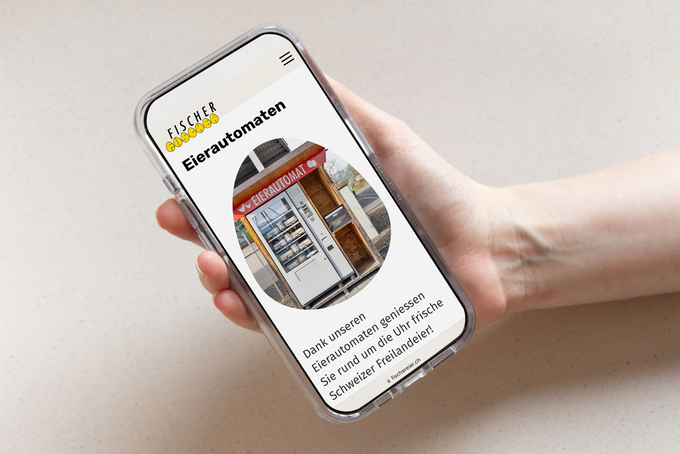 Eine Hand hält ein Smartphone, auf dem eine Webseite zum Thema Eierautomaten angezeigt wird. Zu sehen ist ein Eierautomat. Der Text unter dem Bild beschreibt den Genuss frischer Eier aus Schweizer Freilandhaltung.