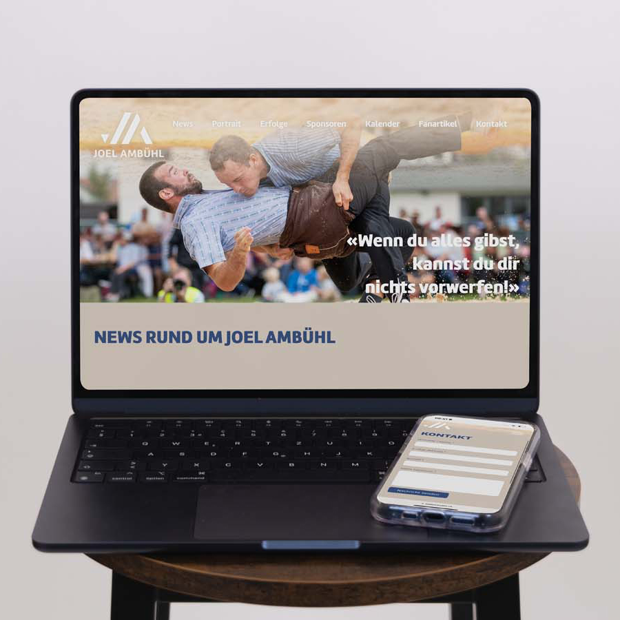 Auf einem runden Tisch steht ein Laptop, auf dem eine Wrestling-Website mit zwei Männern in einem Kampf zu sehen ist. Daneben liegt ein Smartphone mit transparenter Hülle, auf dem Kontaktdaten angezeigt werden.