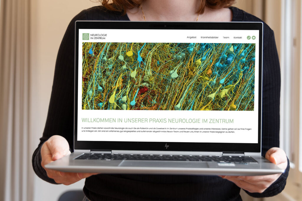 Eine Person hält einen Laptop in der Hand, auf dem eine Webseite mit dem Titel „Neurologie im Zentrum“ angezeigt wird. Der Bildschirm zeigt farbige Neuronenbilder und einen deutschen Text, der Besucher in der neurologischen Praxis willkommen heißt. Verschiedene Navigationslinks sind sichtbar.