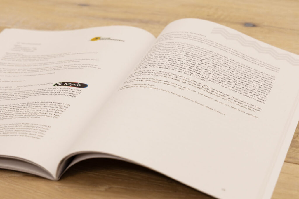 Offenes Buch auf Holzoberfläche. Seiten mit gedrucktem Text und Logos. Die linke Seite enthält ein Keyko-Logo. Die Seiten scheinen Teil eines Dokuments oder Berichts zu sein.