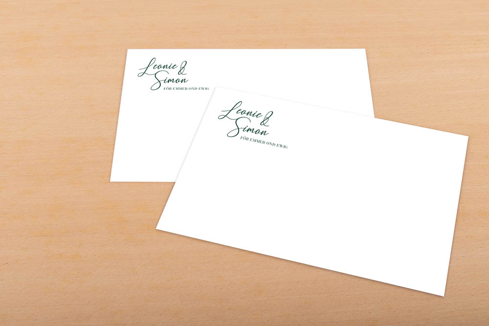 Zwei weiße Briefumschläge mit eleganter grüner Schrift "Leonie & Simon" in der oberen linken Ecke, auf einer hellen Holzunterlage.