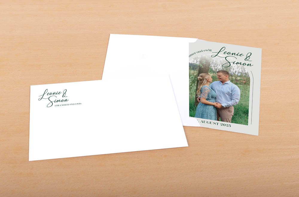 Eine Hochzeitseinladung und ein Umschlag auf einer hellen Holzoberfläche mit dem Foto eines lächelnden Paares und den Namen "Leonie & Simon", August 2025.