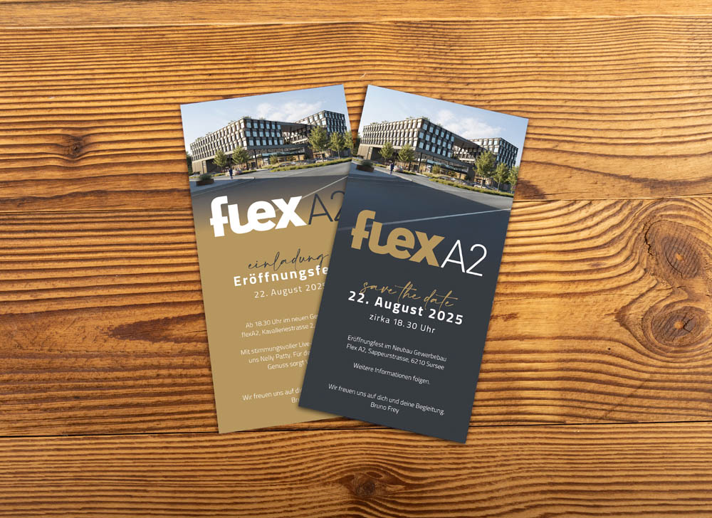 Zwei Einladungskarten für die Veranstaltung "flexA2", mit einem modernen Gebäudefoto und deutschen Details. Karten auf Holzoberfläche; eine gold, eine dunkelgrau.