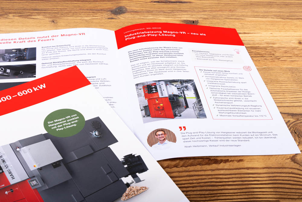 Zwei aufgeschlagene Broschüren mit Bildern und Details über industrielle Heizungssysteme mit deutschem Text, Maschinenfotos und Produktbeschreibungen sind auf einer Holzfläche platziert.