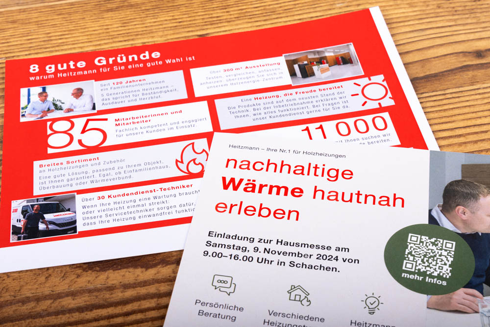 Eine Broschüre und ein Flyer auf einem Holztisch werben für Heiztmann und zeigen Vorteile, Kennzahlen und Dienstleistungen auf. Der Flyer lädt zu einem Tag der offenen Tür am 9. November 2024 in Schachen ein, bei dem nachhaltige Heizlösungen vorgestellt werden.