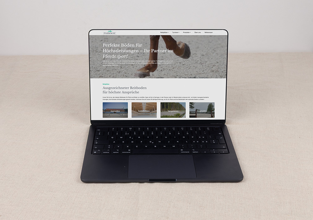 Ein schwarzer Laptop auf einer beigen Oberfläche zeigt eine Website über Premium-Reitböden mit Bildern von Reitplätzen und Pferdeanlagen. Der Bildschirm zeigt deutschen Text und verschiedene Navigationsregisterkarten am oberen Rand.