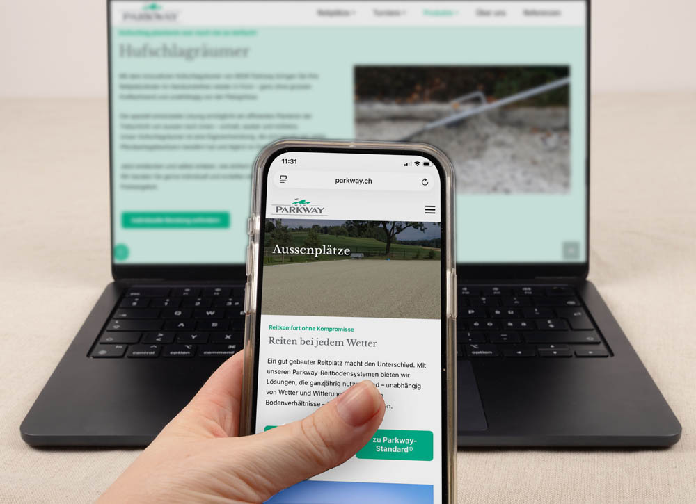 Eine Hand hält ein Smartphone, auf dem eine Website angezeigt wird, während ein Laptop dieselbe Website unscharf im Hintergrund anzeigt. Beide Bildschirme zeigen Inhalte über Reitplätze in deutscher Sprache.