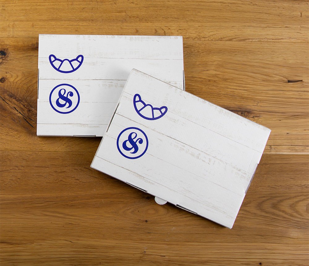 Zwei weiße rechteckige Kästen mit einfachen blauen Hörnchen- und kaufmännischen Symbolen stehen auf einer Holzfläche. Die Kästchen haben ein strukturiertes, hölzernes Plankenmuster und sind leicht überlappend angeordnet.