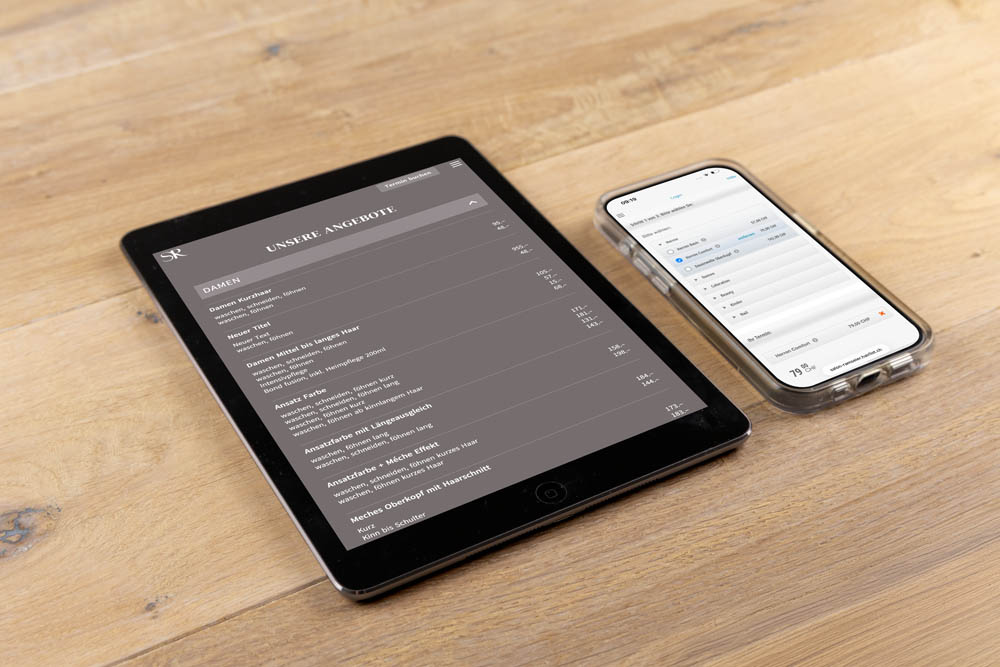 Ein Tablet und ein Smartphone liegen auf einer Holzoberfläche. Das Tablet zeigt eine Speisekarte in deutscher Sprache mit verschiedenen Gerichten und Preisen an, während das Smartphone eine Terminplan- oder Kalender-App anzeigt.