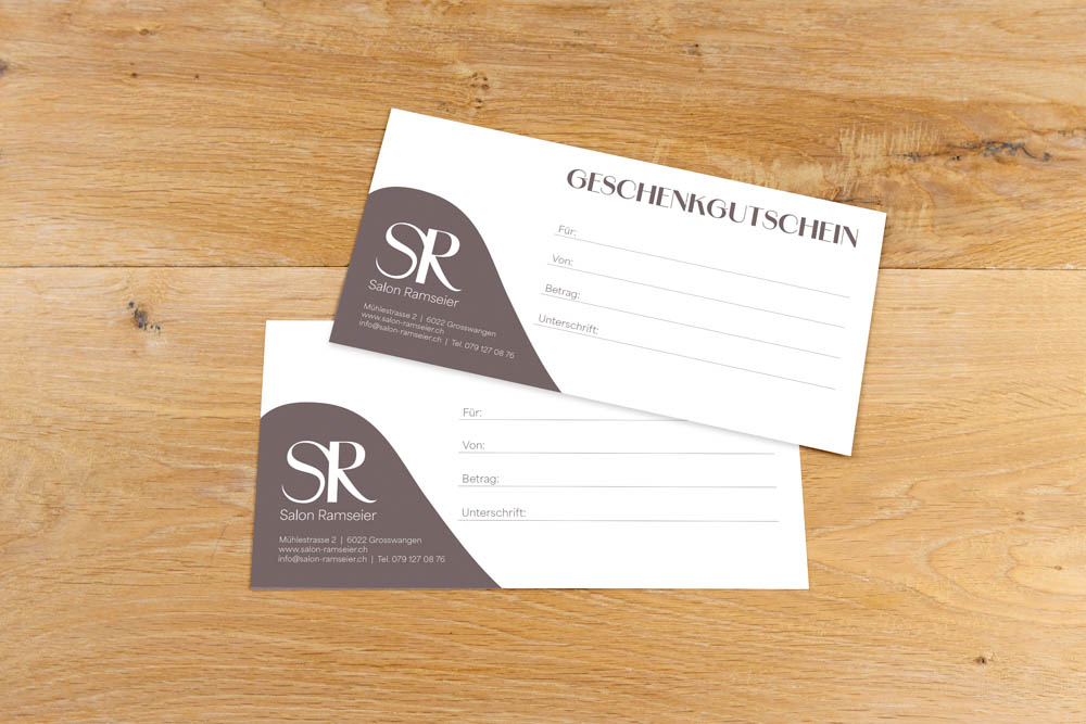 Zwei Geschenkgutscheine von "Salon Ramseier" sind auf einer Holzfläche ausgestellt. Die Karten sind in Braun und Weiß gehalten und bieten Platz für den Empfänger, den Absender, den Betrag und die Unterschrift.
