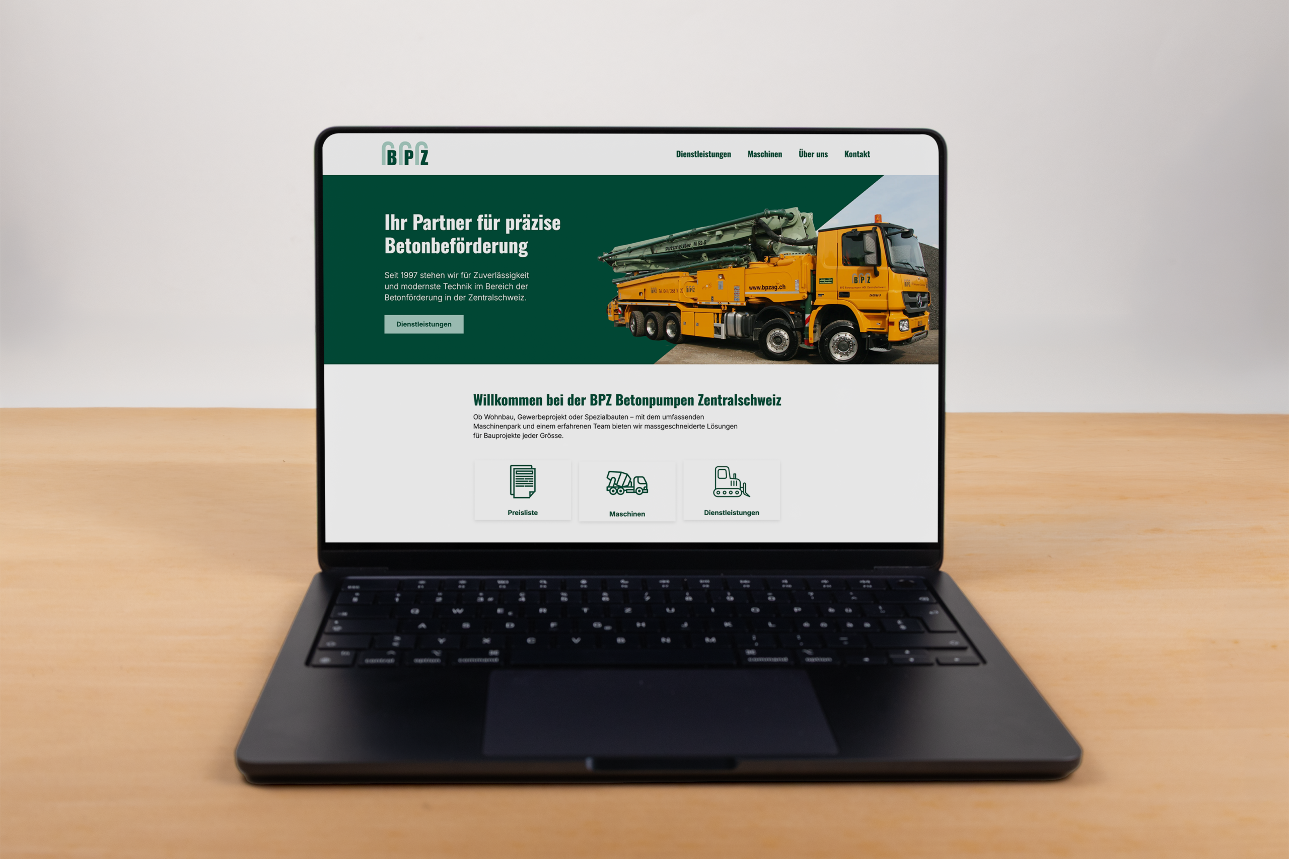 Ein Laptop auf einem Holztisch zeigt eine Website von BPZ Betonpumpen Zentralschweiz mit einem gelben Betonpumpen-LKW und Navigationsoptionen wie "Produkte", "Mieten" und "Dienstleistungen".