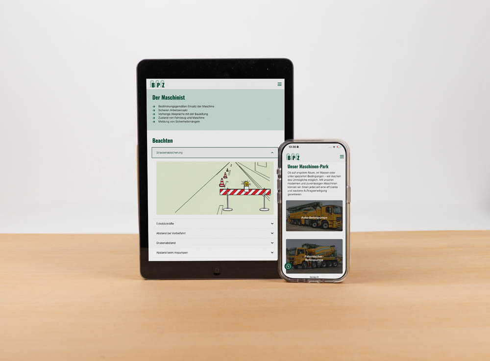Ein Tablet und ein Smartphone werden auf einer Holzoberfläche angezeigt. Beide Bildschirme zeigen eine Website mit Konstruktionsinhalten in deutscher Sprache.