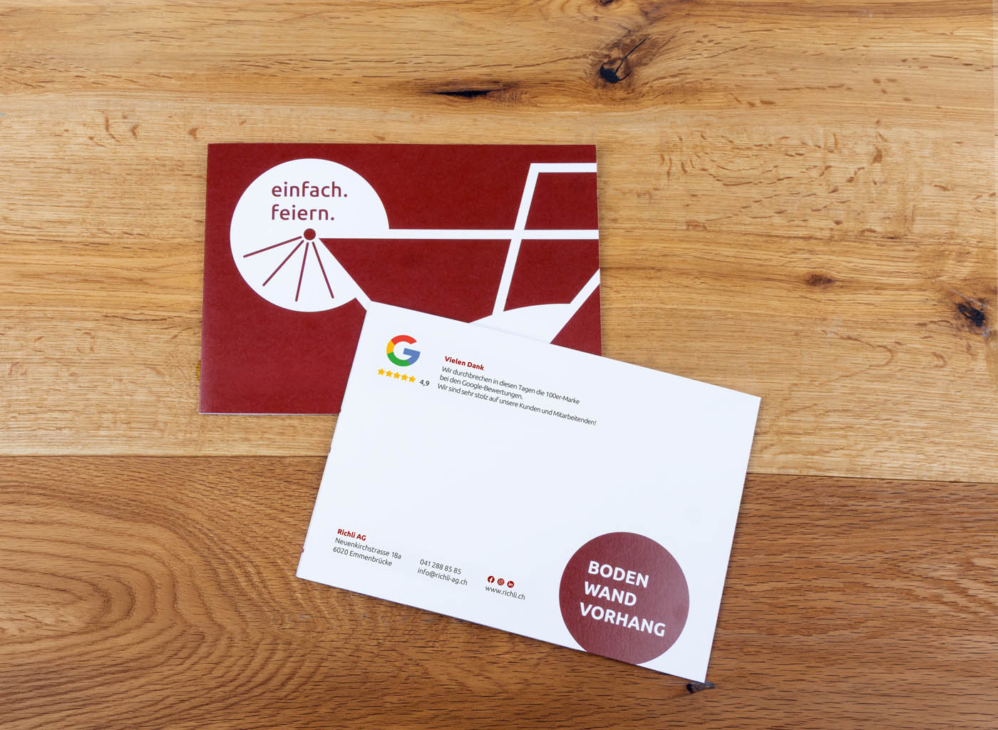 Zwei Postkarten auf einer hölzernen Oberfläche - eine rot mit "einfach. feiern." in Deutsch, eine meist weiß mit buntem Text und einem roten Kreis.